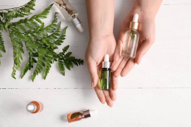 Doğal serumdan şişeler ve hafif ahşap arka planda eğreltiotu yaprağı olan kadın elleri.