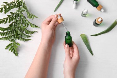 Doğal serumdan şişeler ve hafif ahşap arka planda eğreltiotu yaprağı olan kadın elleri.