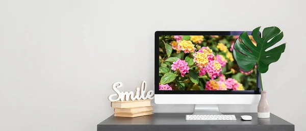 Workplace with computer, tropical leaf in vase and books on light background with space for text