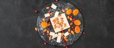 Tatlı beyaz çikolata, badem fıstığı ve koyu arkaplanda kurutulmuş kayısı.