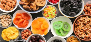 Koyu ahşap arka planda farklı kurutulmuş meyve ve fındıklı kaseler.