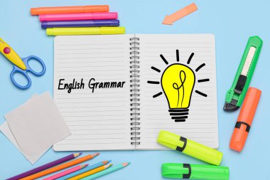 Açık mavi arkaplan üzerinde ENGLISH GRAMMAR ve kırtasiye içeren defter