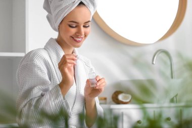 Banyoda elinde hindistan cevizi yağı şişesi olan genç bir kadın.