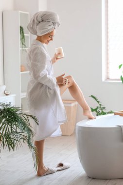 Genç bir kadın banyoda bacağına hindistan cevizi yağı sürüyor.