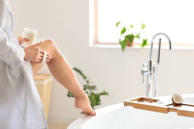 Genç bir kadın banyoda bacağına hindistan cevizi yağı sürüyor.