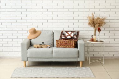 Piknik sepeti, fotoğraf makinesi, çanta ve beyaz tuğla duvarın yanındaki şapka.