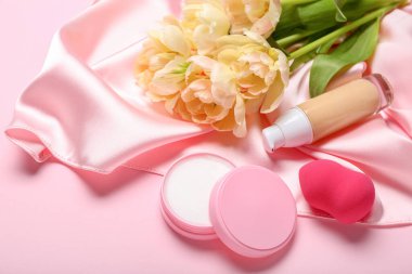 Bir buket lale, dekoratif kozmetik ve pembe arka planda makyaj süngeri.