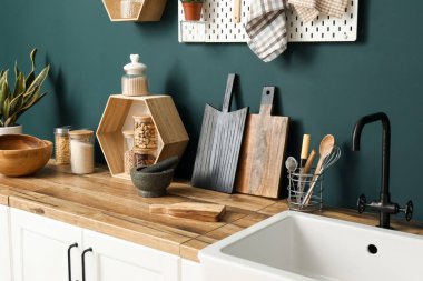 Ahşap tahtalar, mutfak aletleri ve lavabo yeşil duvarın yanında.