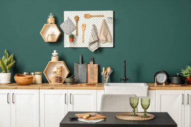 Yemek masası ve mutfak gereçleri yeşil duvarın yanında.