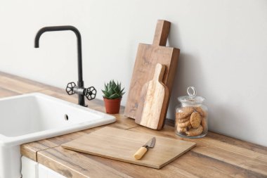 Işık duvarının yanındaki tezgahlarda kurabiye kavanozu, lavabo ve bitki kesme tahtaları.