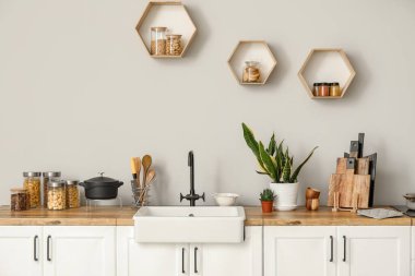 Lavabo, yiyecek, mutfak gereçleri ve ışık duvarının yanındaki ev bitkileriyle dolu beyaz tezgahlar.