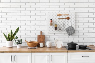 Mutfak gereçleri, soba ve beyaz tuğla duvarın yanındaki ev bitkileriyle tezgahlar.