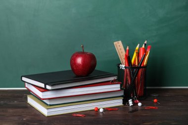 Yeşil karatahtanın yanındaki masada kitap ve elma bulunan okul kağıtları.