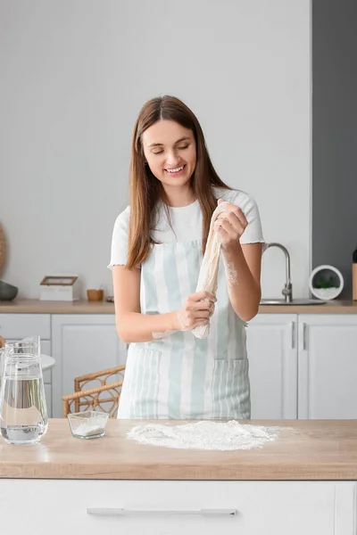 Pretty young woman with raw dough in kitchen