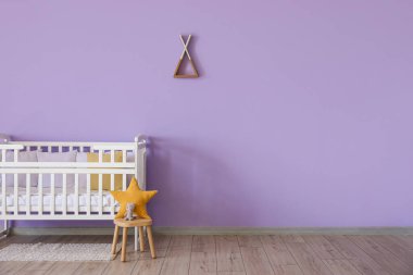 Yastıklı bebek beşiği ve menekşe duvarın yanında tabure.