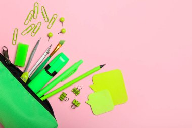 Ataşlı yeşil kalem çantası ve pembe arka planda okul kırtasiyesi