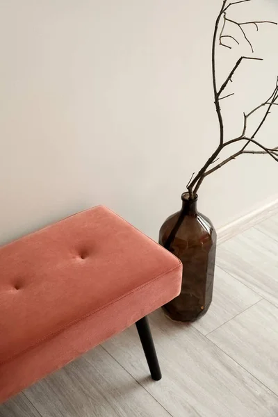 Pink bench and tree branches in vase near light wall