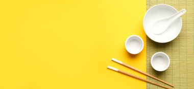 Çin kâselerinde yemek çubukları ve sarı zemin üzerinde bambu hasırı ve metin için yer var.