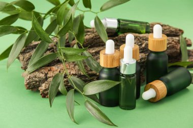 Doğal serum şişeleri, ağaç kabuğu ve bitki yaprakları yeşil arka planda.