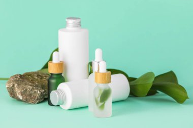 Turkuaz arka planda doğal serum, kozmetik, taş ve bitki yaprakları.