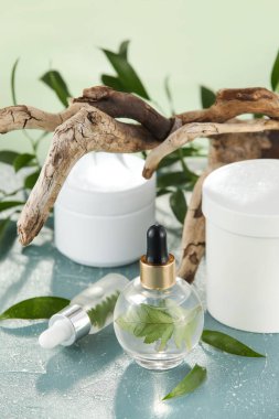 Şişe dolusu doğal serum, ağaç dalları ve yeşil masa üzerindeki bitki yaprakları.