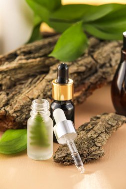 Doğal serum şişeleri, ağaç kabukları ve bitki yaprakları bej masa üzerinde, yakın plan.