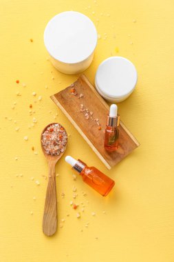 Doğal serumlar, kozmetik ürünleri ve sarı arkaplanda tuz bulunan kaşık.