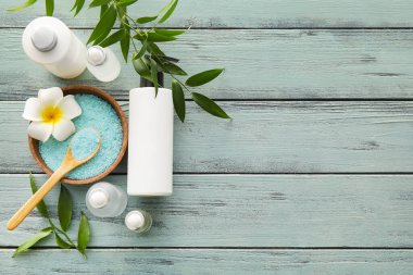 Doğal serum şişeleri, yeşil ahşap arka planda tuz ve bitki yapraklarıyla dolu bir kase.