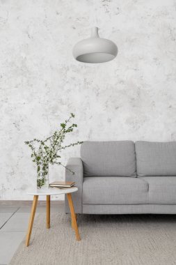 Çiçek açan dalları ve ışık odasındaki kanepenin yanındaki masada kitapları olan vazo.