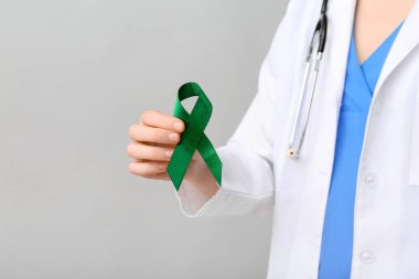 Gri arka planda yeşil kurdeleli kadın doktor, yakın plan. Karaciğer kanseri kavramı