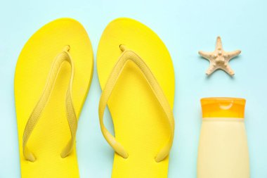 Mavi arka planda deniz yıldızı ve parmak arası terlikli bir şişe güneş kremi.
