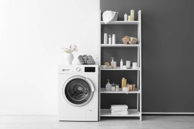 Çamaşır makinesi, vazodaki çiçekler, banyo aksesuarlı raflar siyah beyaz duvarın yanında.