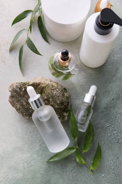 Şişeler dolusu doğal serum, taş, kozmetik ve bitki yaprakları hafif grunge arka planda