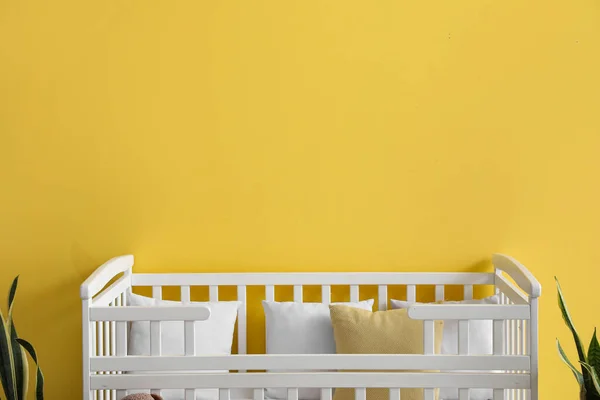 子供部屋の黄色い壁の近くの快適なベビーベッドと観葉植物 — ストック写真