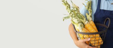 Elinde bir sepet taze mısır koçanı ve açık arkaplan tutan bir kadın.