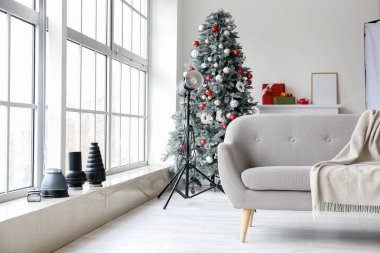 Modern fotoğraf stüdyosunda Noel ağacı, kanepe ve ışıklandırma ekipmanları.