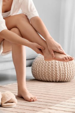 Kanepede oturan ve odada ayak masajı yapan bir kadın.