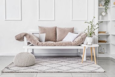 Dizüstü bilgisayarlı kanepe, vazoda çiçek açan dallar masanın üstünde ve ışık duvarının yanında puf.