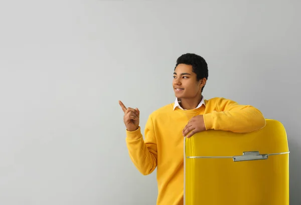 Young African-American guy near stylish yellow fridge pointing at something on grey background