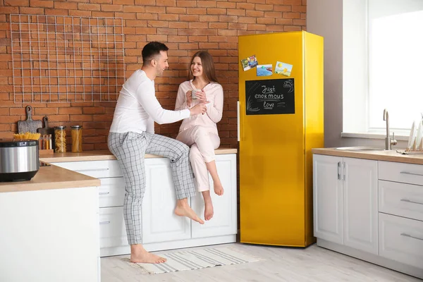 幸せな若いですカップルでパジャマ飲料コーヒー近く冷蔵庫でキッチン — ストック写真