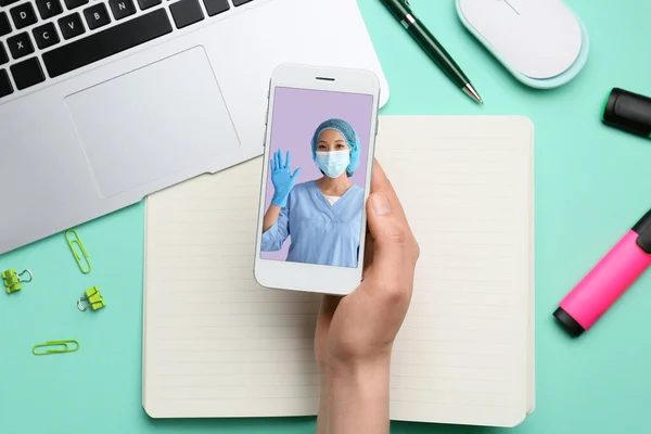 Woman holding smartphone with doctor on screen at table, top view. Concept of telemedicine