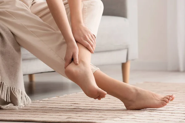 Woman sitting on sofa and making foot massage in room, closeup