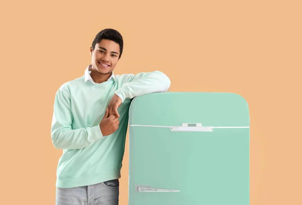 Smiling African-American guy near stylish vintage fridge on color background