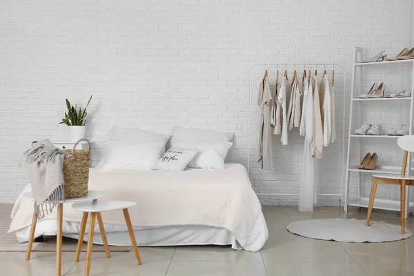 Interior of light bedroom with stylish clothes and shoes