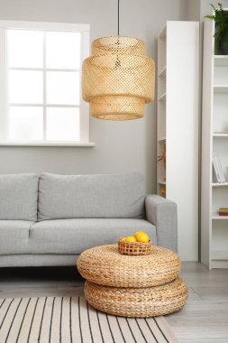 Rahat bir kanepe ve modern bir lamba. Odada rattan puf var.