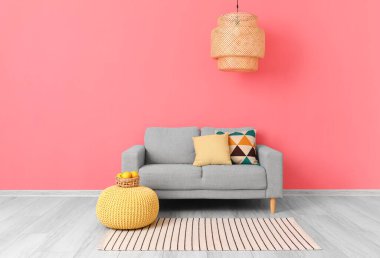 Pofuduk ve şık lambalı rahat bir kanepe, pembe duvarın yanında.