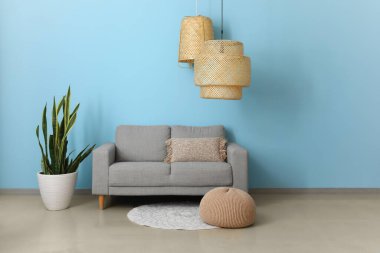 Rahat bir kanepe, çiçek ve mavi duvarın yanında şık bir lamba.