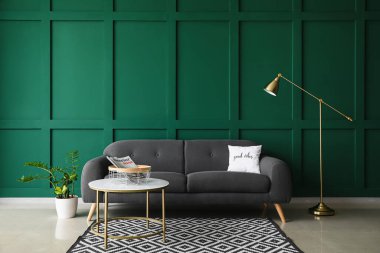 Masası ve yeşil duvarın yanında modern lambası olan rahat bir kanepe.