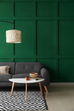 Masası ve yeşil duvarın yanında modern lambası olan rahat bir kanepe.