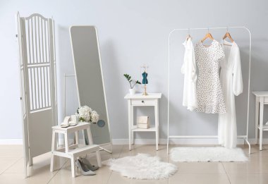 Şık kadın kıyafetleri, masa, merdiven ve aynayla aydınlık duvarın yanında dizilin.